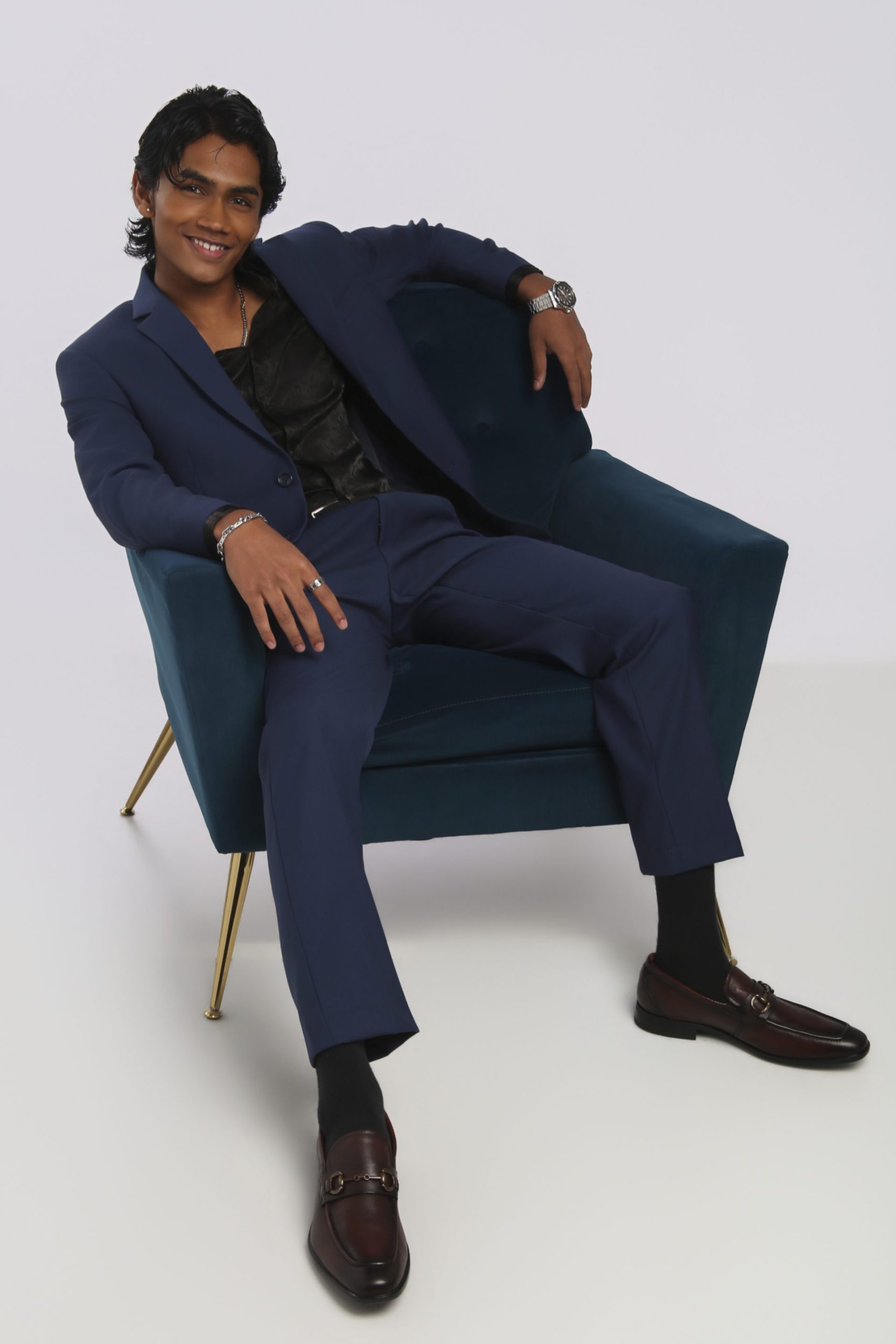 Shabs seated in a teal armchair wearing a navy suit