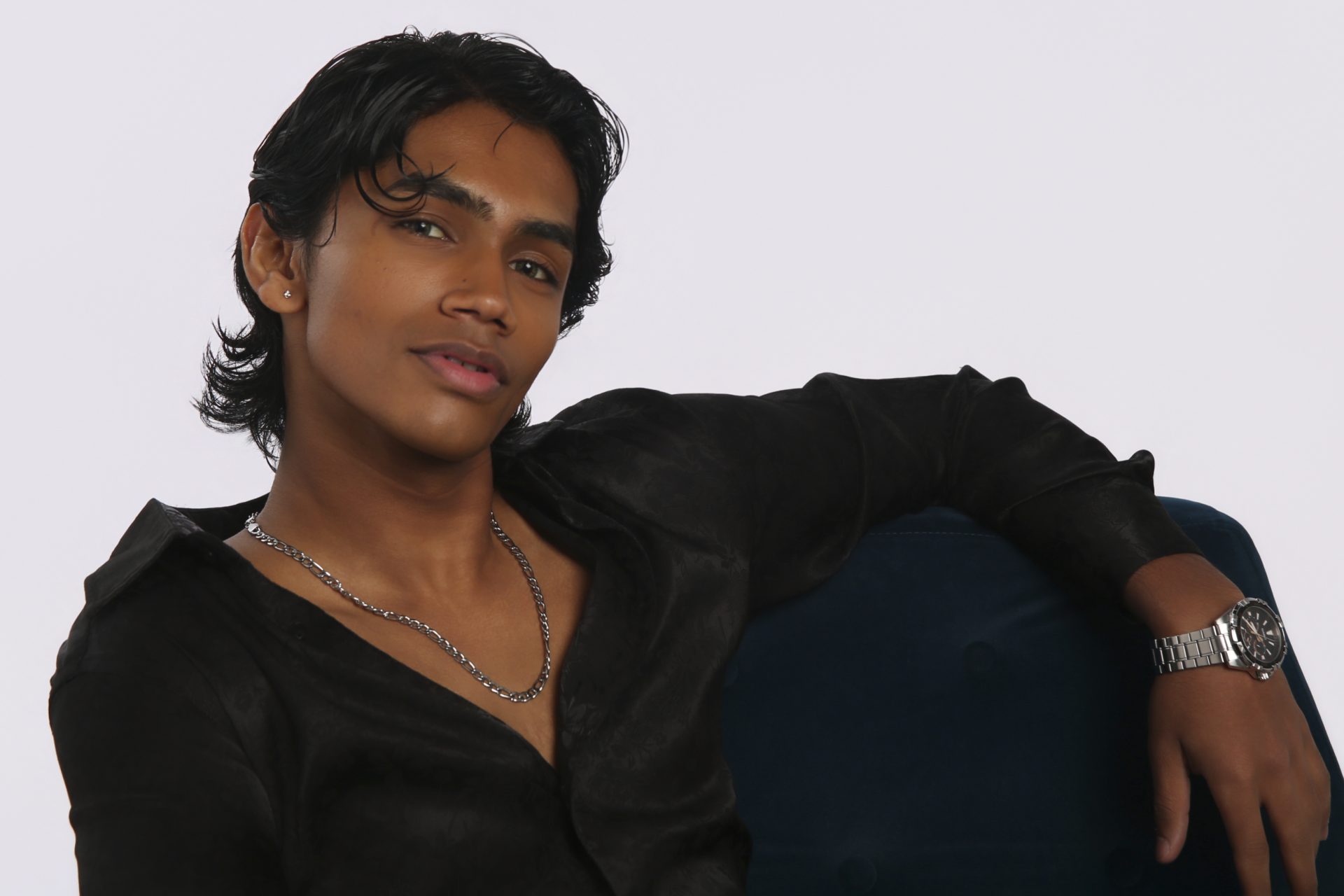 Shabs reclining against a blue armchair in an open black shirt