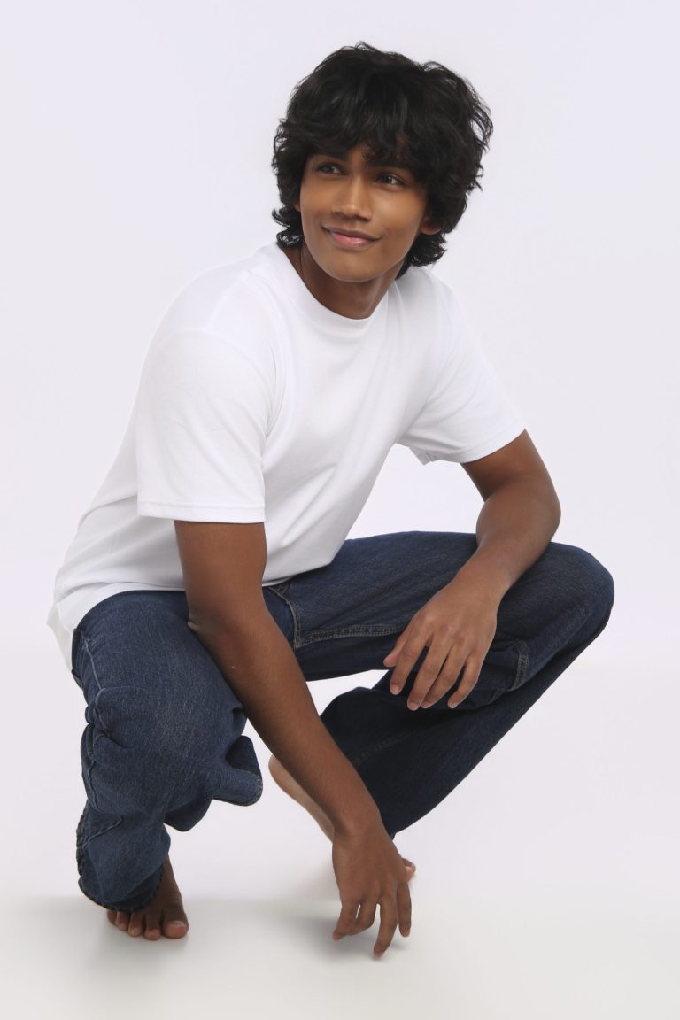 Shabs crouching in a white tee and denim, smiling